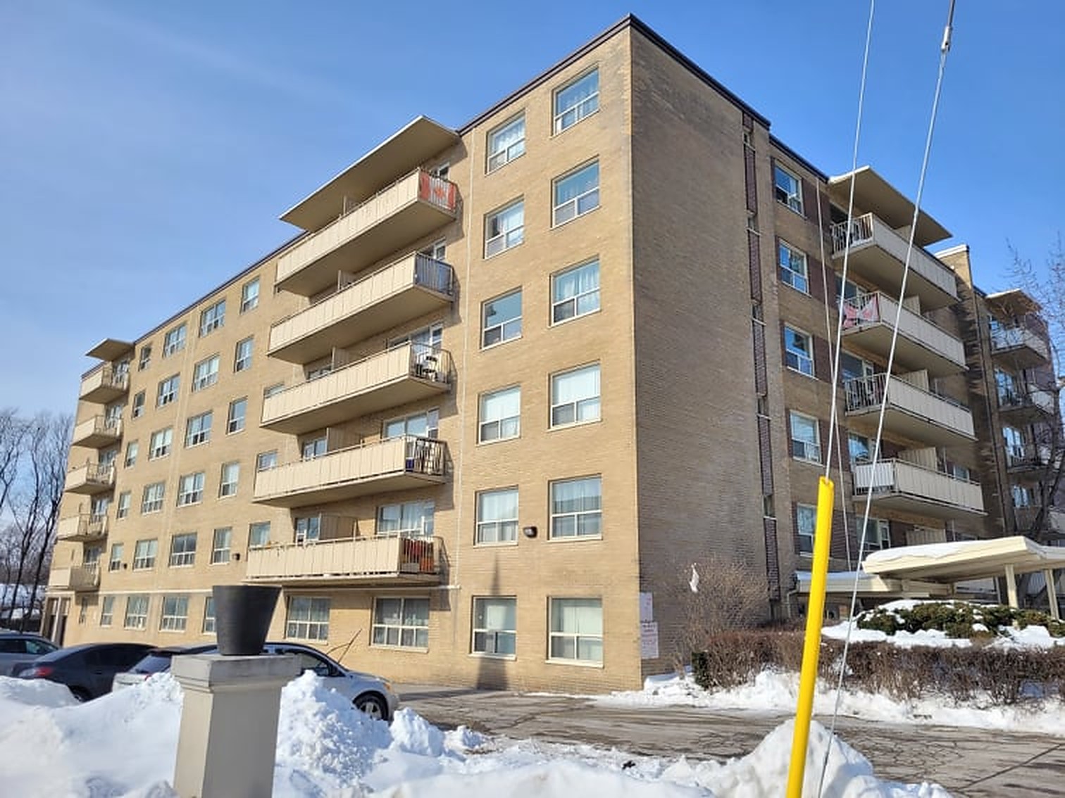 Six-storey mid-century buff-brick apartment building with projecting concrete balconies on a clear winter day